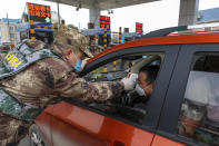 FILE - In this Jan. 23, 2020, file photo, a militia member uses a digital thermometer to take a driver's temperature at a checkpoint at a highway toll gate in Wuhan in central China's Hubei Province. The Chinese city of Wuhan is looking back on a year since it was placed under a 76-day lockdown beginning Jan. 23, 2020. (Chinatopix via AP, File)