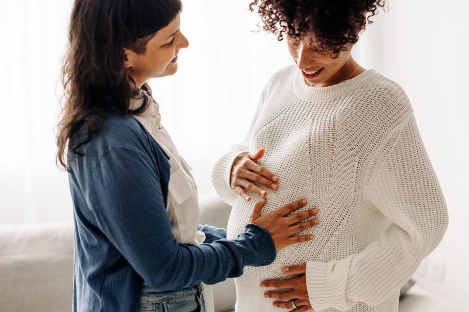 Woman touching another woman's baby bump. (Getty Images)