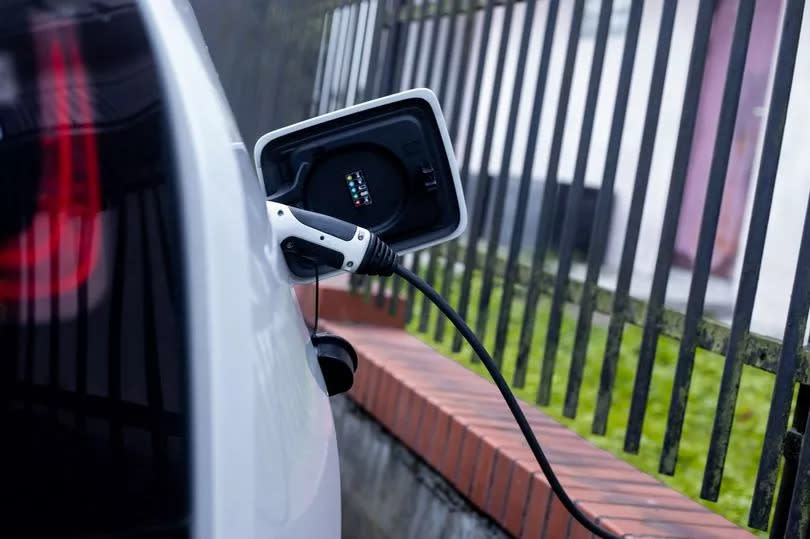 Photo of side of white car with charging equipment plugged in during electric battery charging at home in backyard to take advantage of faster charging speed