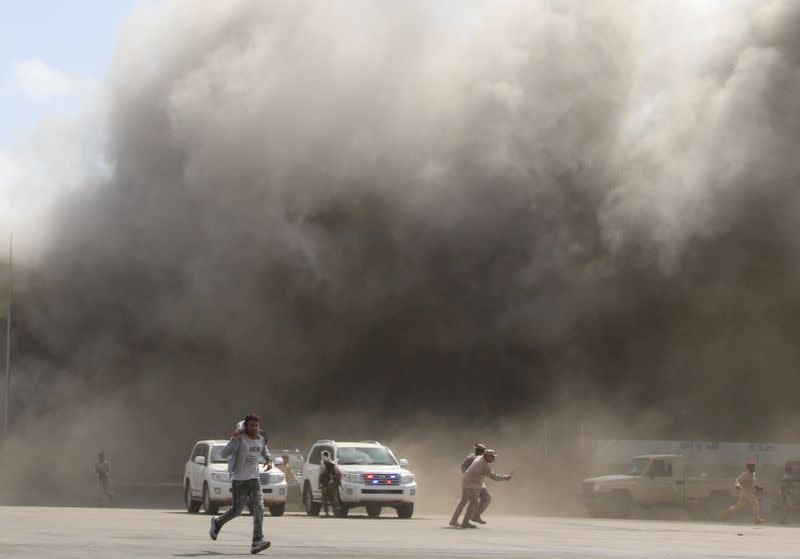 People react as dust rises after explosions hit Aden airport, upon the arrival of the newly-formed Yemeni government in Aden