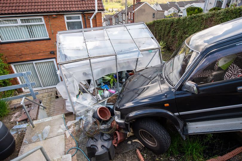 A black 4x4 rests against a partly-demolished greenhouse