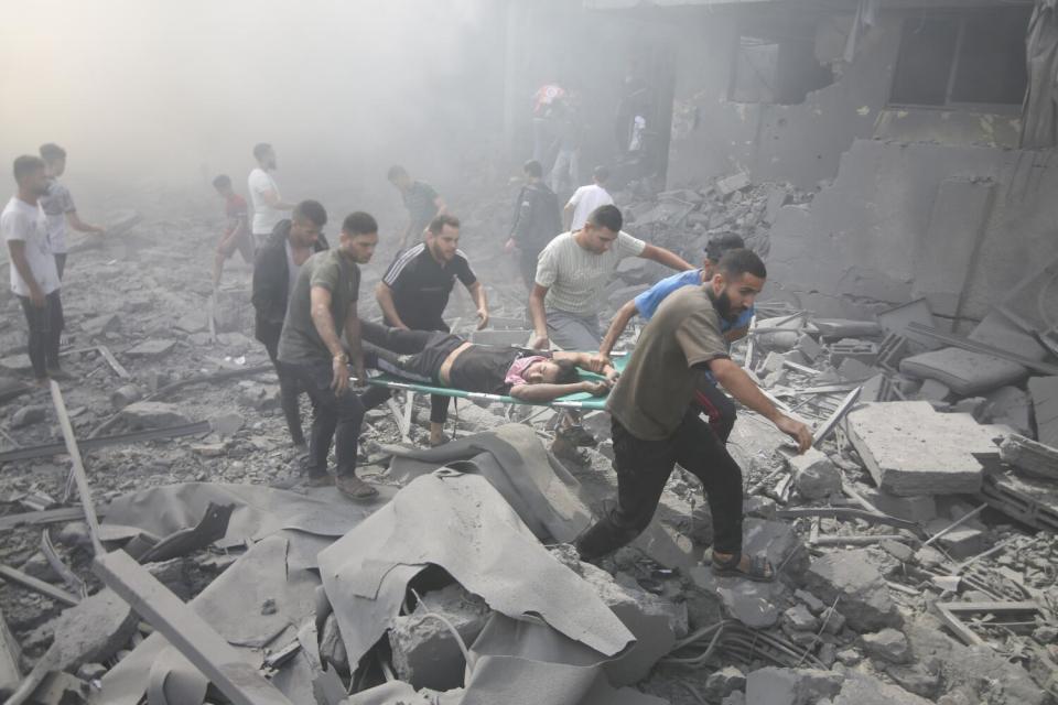 Men carry a person on a stretcher over rubble.