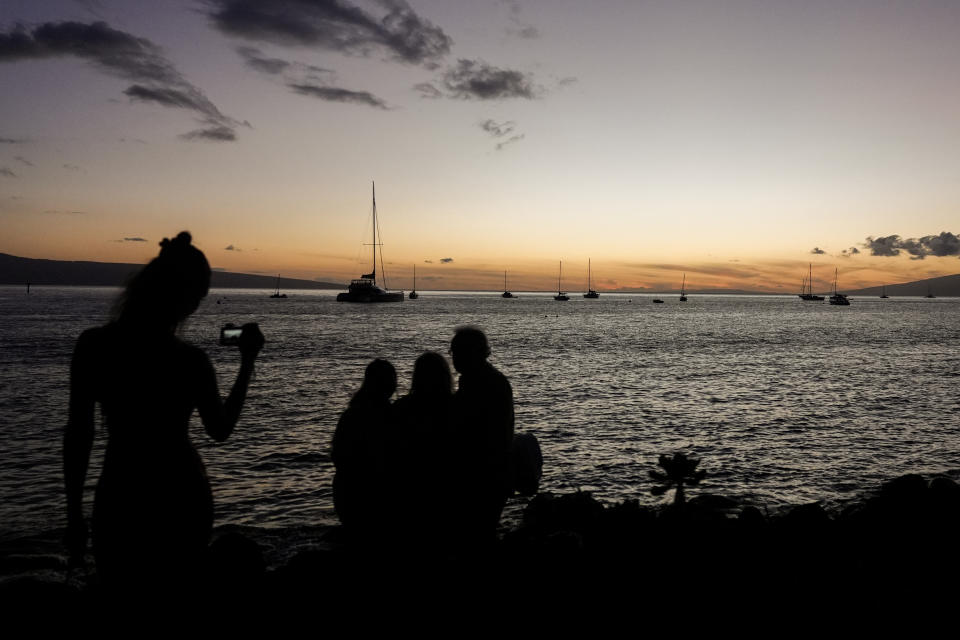 Tourists take photos near the water on a reopened area of Front Street, Friday, July 5, 2024, in Lahaina, Hawaii. Cleanup and rebuilding efforts continue after the 2023 wildfire that killed over 102 people and destroyed the historic town of Lahaina on the island of Maui. (AP Photo/Lindsey Wasson)