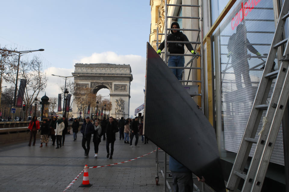A workers protects a shop a window on the Champs-Elysees avenue in Paris, Friday, Dec.14, 2018. Anticipating a fifth straight weekend of violent protests, Paris' police chief said Friday that armored vehicles and thousands of officers will be deployed again in the French capital this weekend. (AP Photo/Francois Mori)