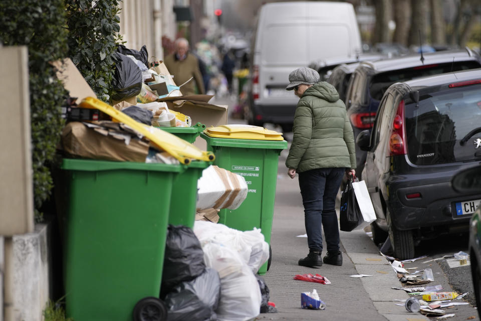 A woman walks past uncollected garbages in Paris, Thursday, march 23, 2023. French unions are holding their first mass demonstrations Thursday since President Emmanuel Macron enflamed public anger by forcing a higher retirement age through parliament without a vote. (AP Photo/Christophe Ena)
