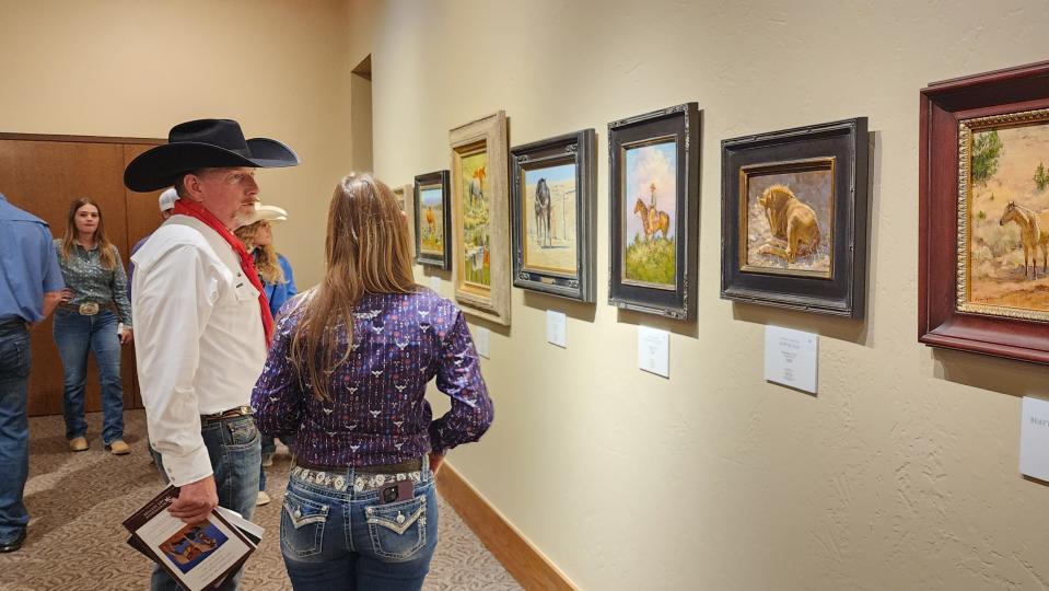 A couple of attendees look over artwork at the AQHA Art Show Aug. 12 in Amarillo.