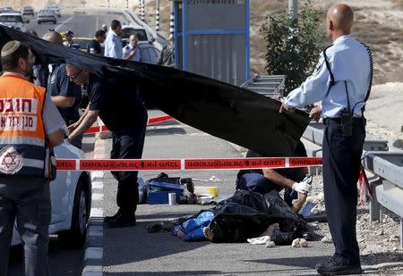 An Israeli police forensics expert touches the covered body of a Palestinian, who police said attempted a ramming attack, near the West Bank Jewish settlement of Kfar Adumim November 22, 2015. REUTERS/Ronen Zvulun TEMPLATE OUT