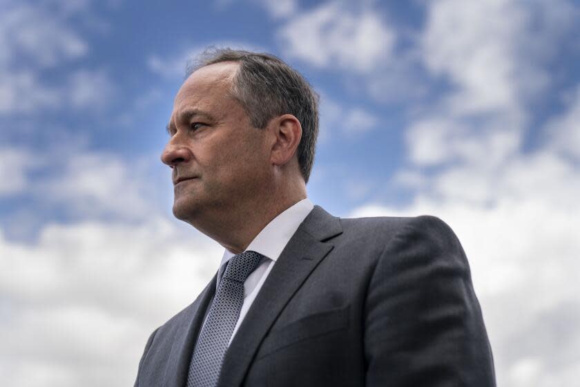 A head-and-shoulders Doug Emhoff looks off to the left of the frame; with sky with white clouds as the background.