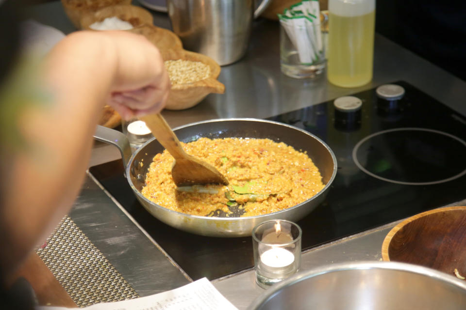 A person stirs food in a pan on a stove. Cooking ingredients and a lit candle are near the pan