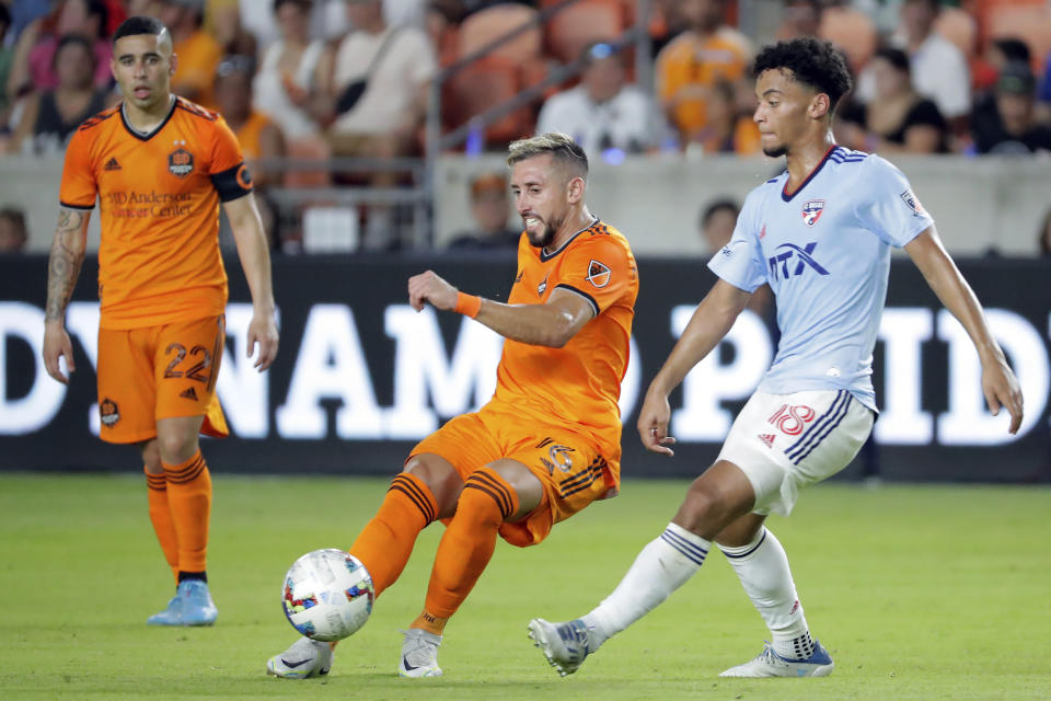 Houston Dynamo's Matias Vera (22) looks on as teammate Hector Herrera, center, kicks away the ball in front of FC Dallas midfielder Brandon Servania (18) during the second half of an MLS soccer match Saturday, July 9, 2022, in Houston. (AP Photo/Michael Wyke)