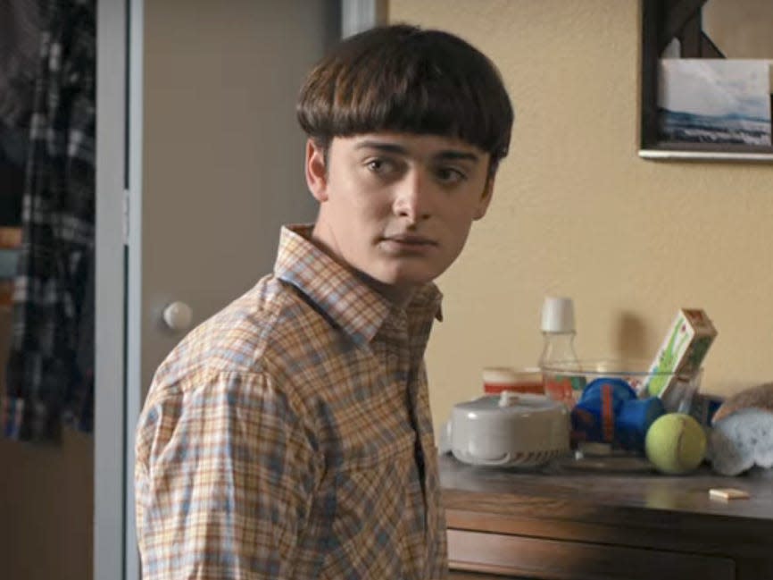 A teenage boy kneeling on the ground in front of a dresser.