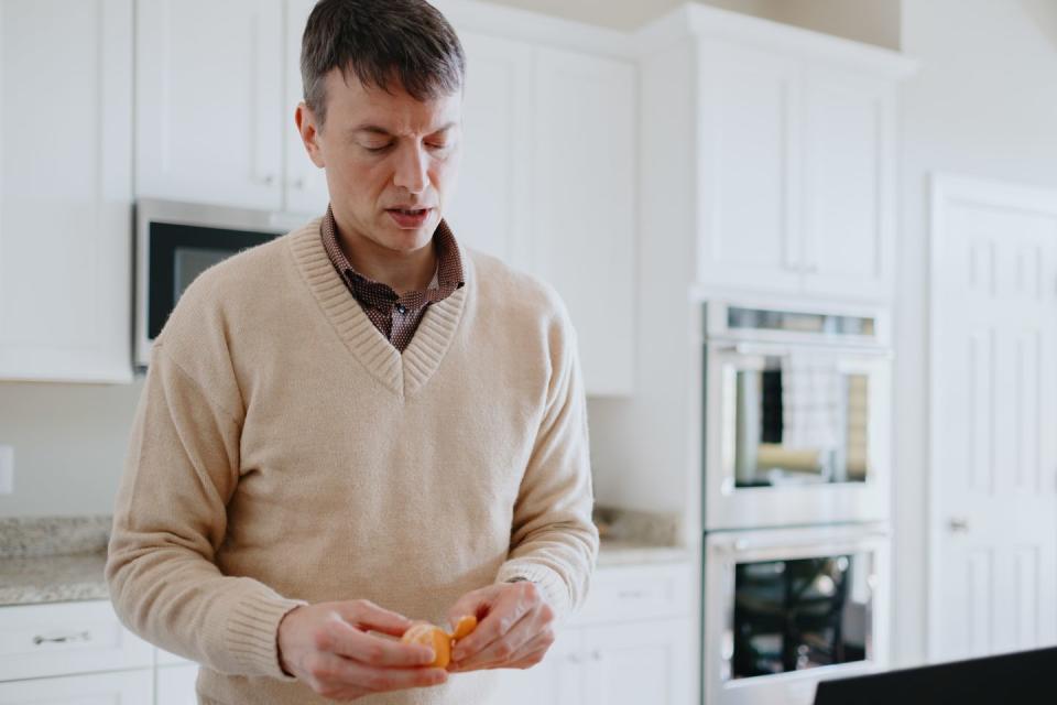 man stands in kitchen peeling a clementine