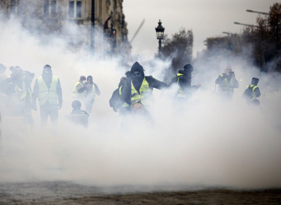 Masked demonstrators wearing yellow jackets appear through tear gas near the Champs-Elysees avenue during a demonstration Saturday, Dec. 1, 2018 in Paris. French authorities have deployed thousands of police on Paris' Champs-Elysees avenue to try to contain protests by people angry over rising taxes and Emmanuel Macron's presidency. (AP Photo/Kamil Zihnioglu)