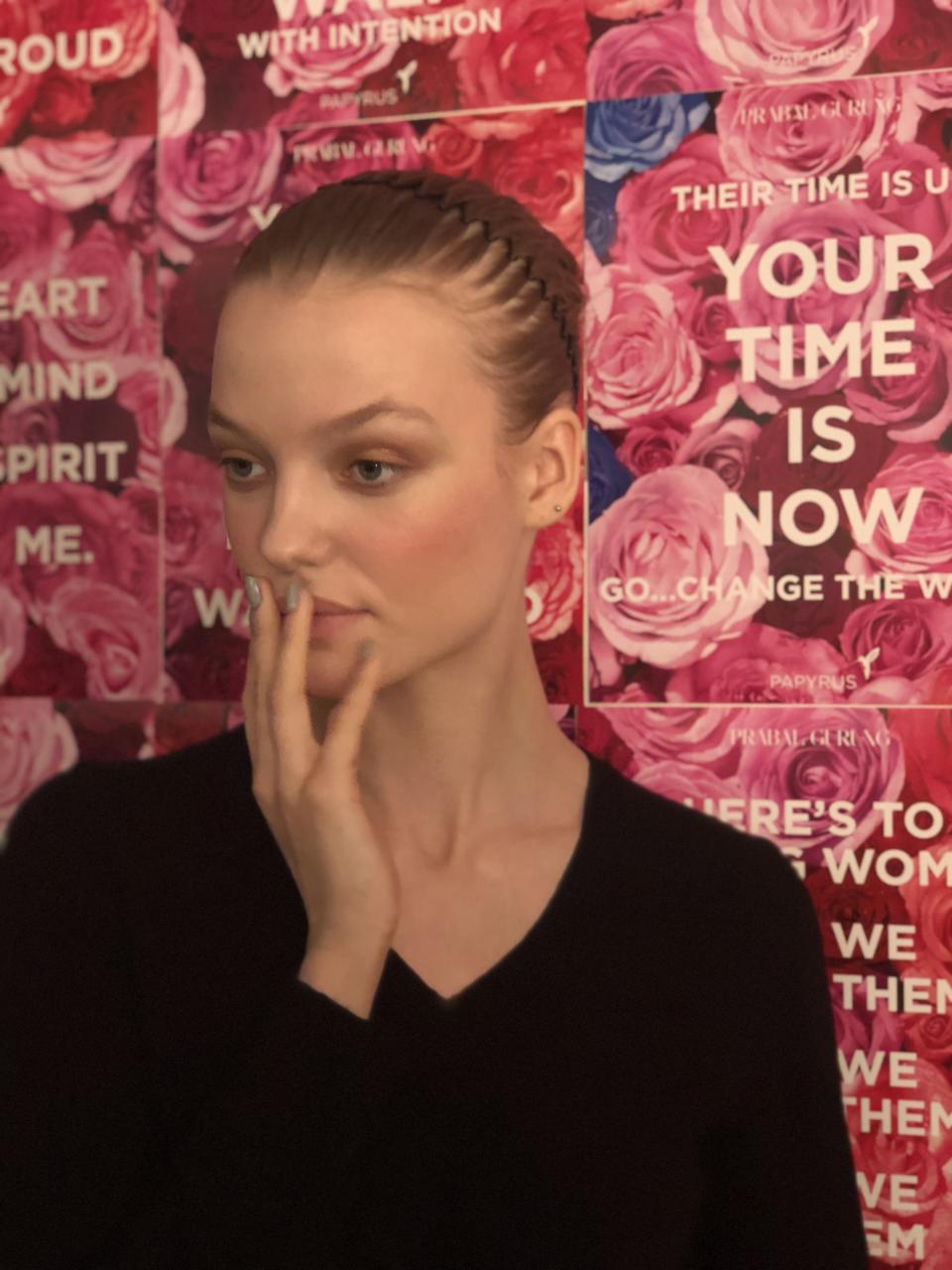 Backstage in hair and makeup, a model poses to show off her beauty look for the Prabal Gurung show in front of a backdrop of empowering messages. (Photo: Alexandra Mondalek)