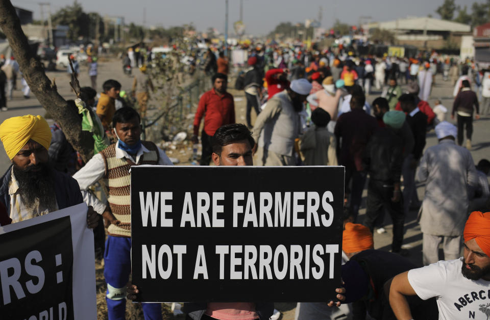 FILE - In this Saturday, Nov. 28, 2020, file photo, a farmer holds a placard on a major highway, blocking traffic as they protest new farm laws, at the Delhi-Haryana state border, India. Farmers form the most influential voting bloc in India — and have long been romanticized as the heart and soul of the nation. Even though agriculture supports more than half of the country’s 1.4 billion people, the economic clout of farmers has diminished over the last three decades. (AP Photo/Altaf Qadri, File)