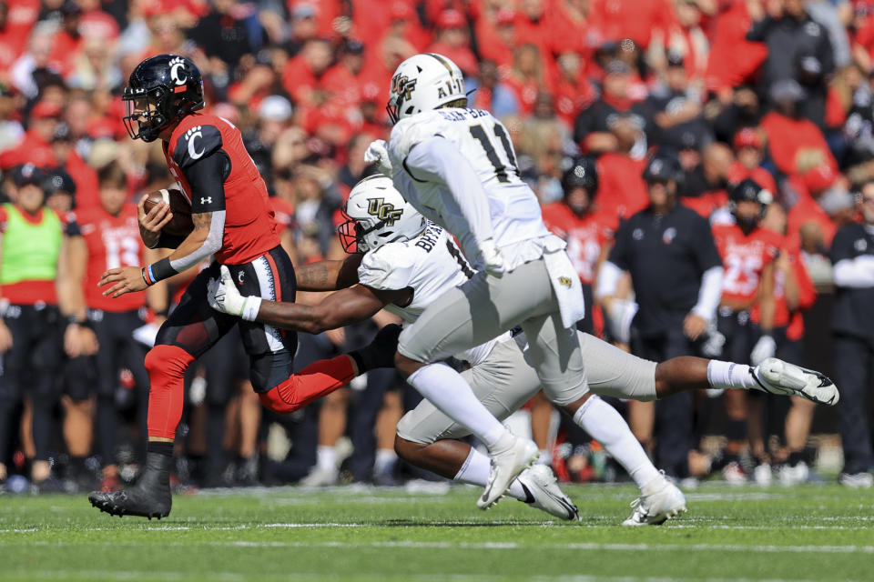 Cincinnati quarterback Desmond Ridder, left, carries the ball as he is tackled by UCF defensive lineman Big Kat Bryant (1) during the first half of an NCAA college football game, Saturday, Oct. 16, 2021, in Cincinnati. (AP Photo/Aaron Doster)