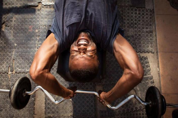 A man trying to life a bar bell in the gym. He has a strained expression on his face.