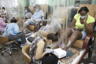 Candace Sanders, right, sits behind a plastic curtain while getting a pedicure at HT&V Nails in the Harlem section of New York, Monday, July 6, 2020. Nail salons and dog runs were back in business on Monday as New York City entered a new phase in the easing of coronavirus restrictions, but indoor restaurant dining will be postponed indefinitely in order to prevent a spike in new infections. (AP Photo/Seth Wenig)