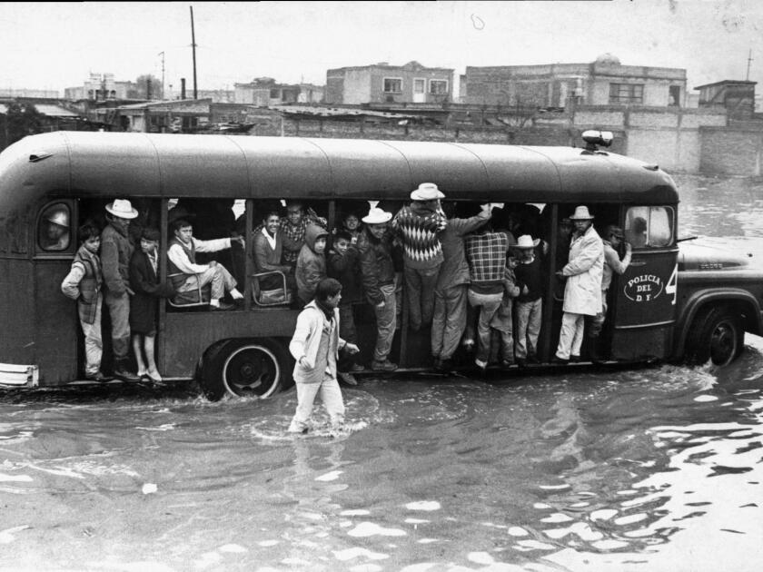 Archival photograph of people holding onto a bus or walking through flooded streets of Mexico City. 