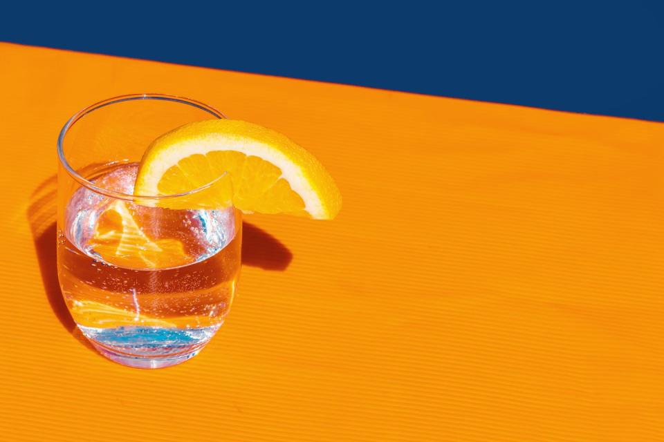 studio shot of glass of club soda with slice of lemon on an orange background