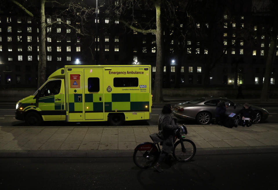 A woman with a bicycle walks past an ambulance and members of the media on the north bank of the River Thames opposite the London Eye ferris wheel by the River Thames in London, Thursday, Dec. 31, 2020. The London Eye is one of the traditional sites for New Year's Eve firework display, but it has been cancelled due to the ongoing coronavirus pandemic and the restrictions in place to try and stop its spread. (AP Photo/Matt Dunham)