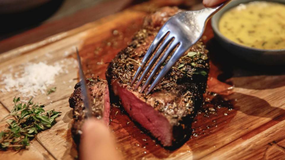 foods for healthy gums: Close up females hands cut a slice of medium rare steak meat. The unrecognizable woman eating dinner in a high end restaurant.