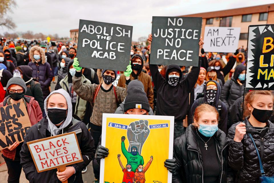 People gather holding signs before curfew April 12, 2021, to protest the death of Daunte Wright, who was shot and killed by a police officer in Brooklyn Center, Minn.