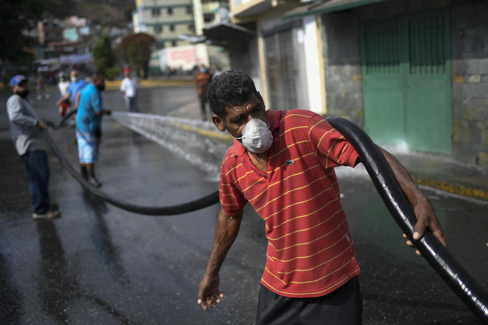 A man holds a hose during a cleaning and disinfection day organized by the Integral Defense Organization, communal council and pro-government groups known as "Colectivos" at the 23 de Enero neighborhood of Caracas, Venezuela, Wednesday, April 29, 2020, during a government-imposed quarantine to help stop the spread of the new coronavirus. (AP Photo/Matias Delacroix)