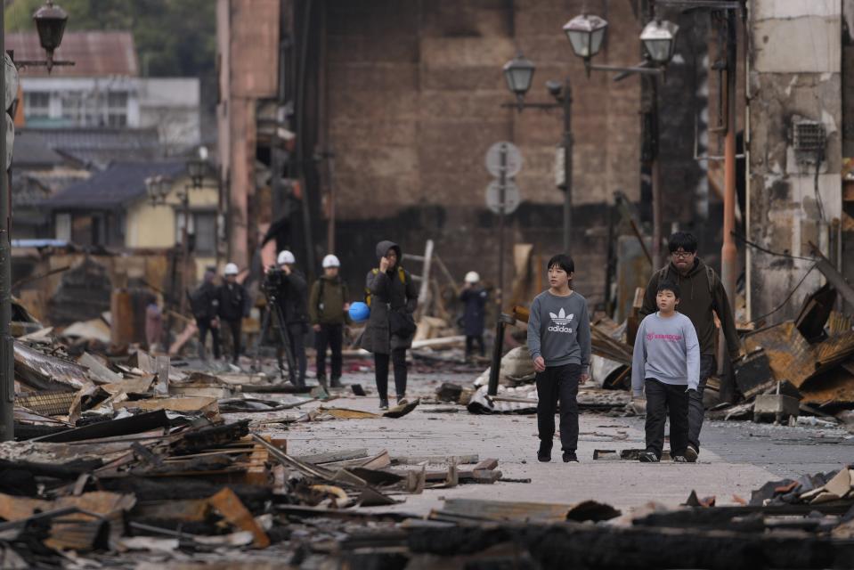 People walk through debris after a fire at a shopping area in Wajima in the Noto peninsula, facing the Sea of Japan, northwest of Tokyo, Friday, Jan. 5, 2024, following Monday's deadly earthquake. (AP Photo/Hiro Komae)