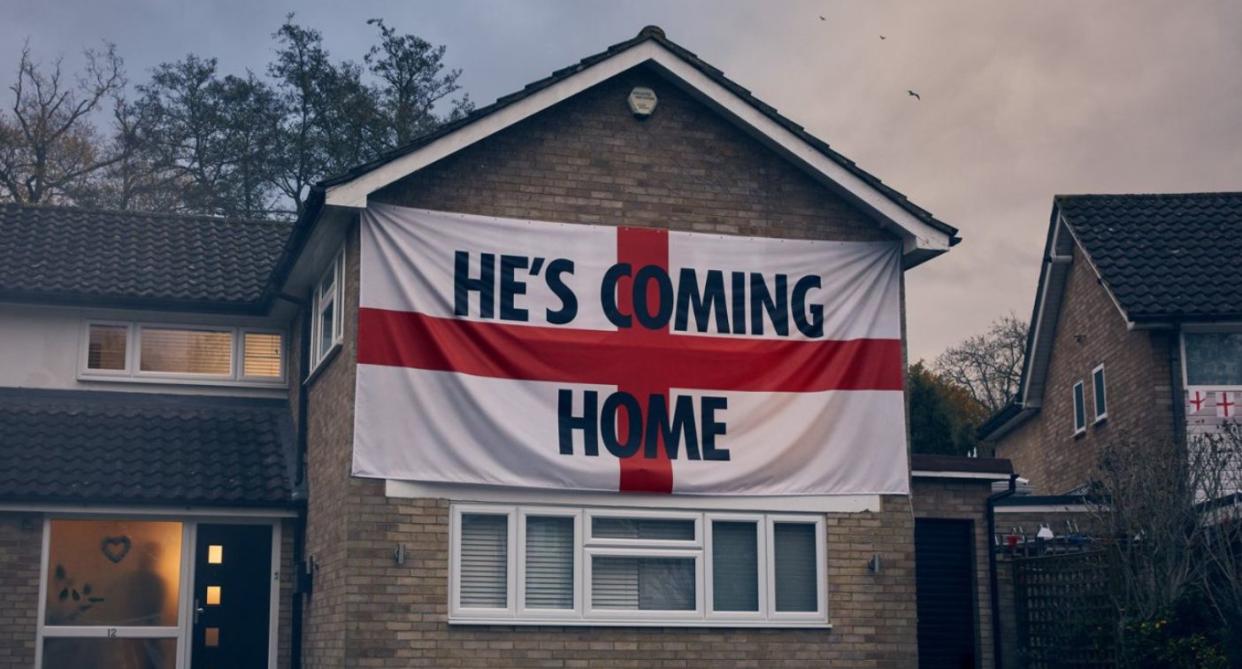 New Women's Aid domestic abuse campaign shows enlarged England flag hanging on side of house with text reading 'he's coming home'. (Women's Aid)