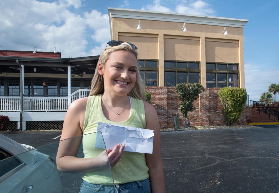 Server Deanna Hall holds her final paycheck from Pensacola's Saltgrass Steak House on March 23. A sign on the door informs customers that the location has permanently closed.