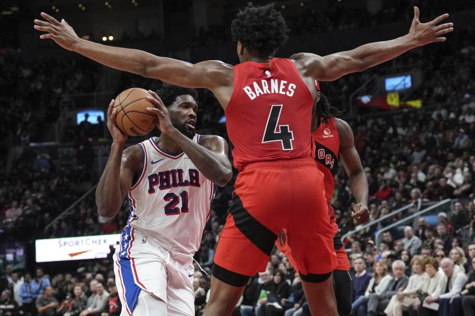 Philadelphia 76ers' Joel Embiid drives between Toronto Raptors' Scottie Barnes and Precious Achiuwa during the second half of an NBA basketball game Saturday, Oct. 28, 2023, in Toronto. (Chris Young/The Canadian Press via AP)