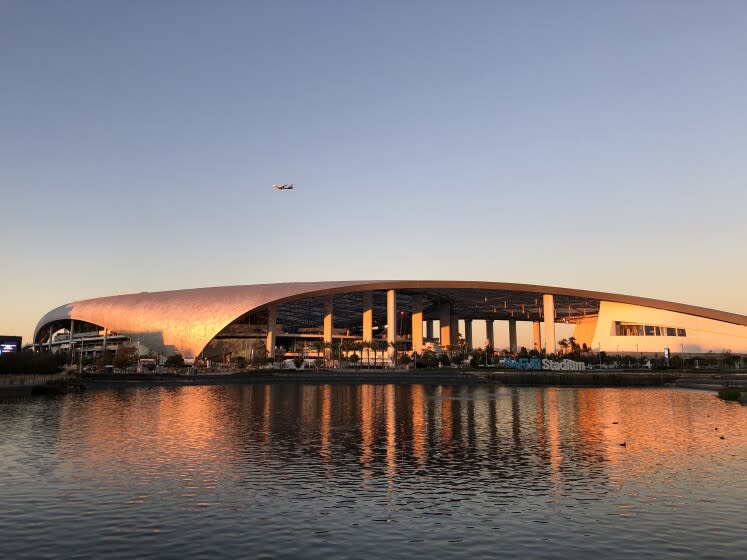 SoFi Stadium's gently curving roof seem to curl into the water of the lake in Lake Park