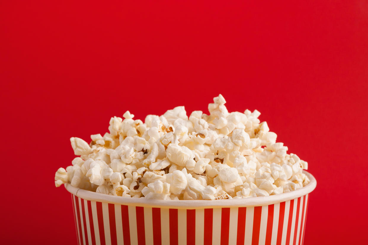 Popcorn in classic striped bukcet on red background. Fluffy maise paper box, copy space. Fast food and movie snack, entertainment concept