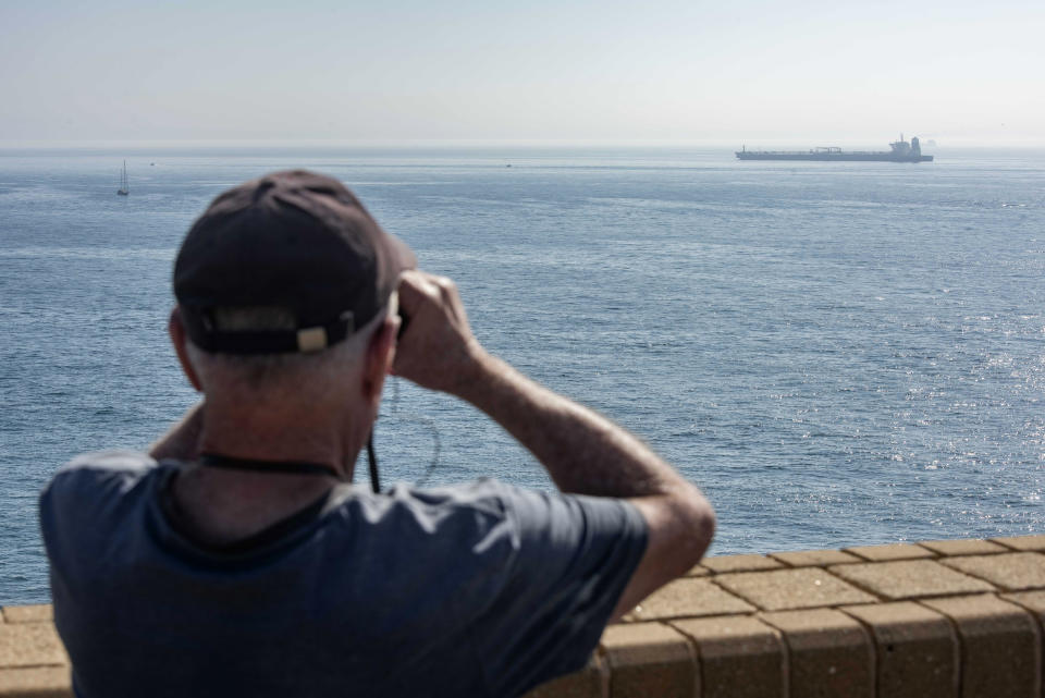 A man uses binoculars to view the Grace 1 supertanker in the British territory of Gibraltar, Friday, Aug. 16, 2019. The lawyer representing the captain of the Iranian supertanker caught in a diplomatic standoff said Friday that the captain no longer wants to be in command of the ship, which is in need of repairs that could prevent its immediate departure from Gibraltar.(AP Photo/Marcos Moreno)