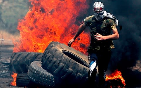 A Palestinian protester runs for cover while being chased by Israeli security forces during a weekly demonstration against the expropriation of Palestinian lands by Israel in the village of Kfar Qaddum - Credit: JAAFAR ASHTIYEH / AFP