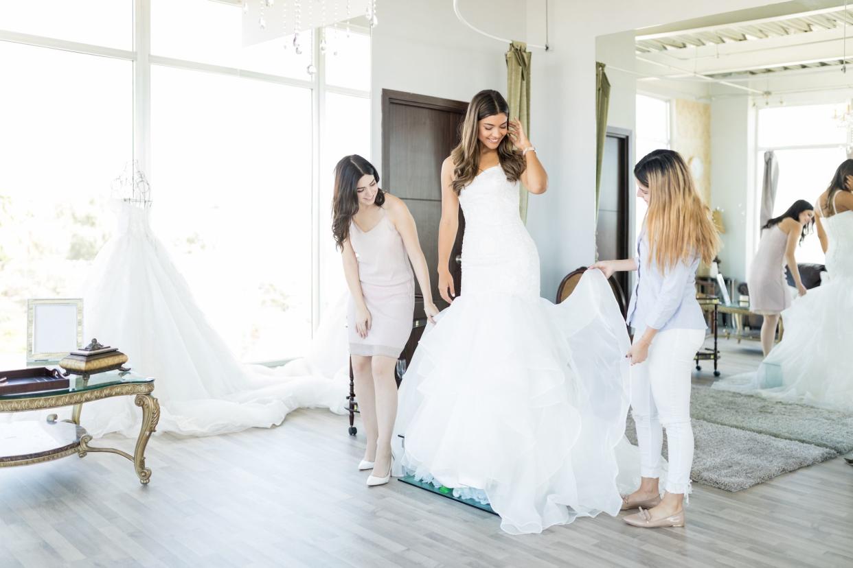 Female customers checking out dress worn by beautiful friend in bridal shop