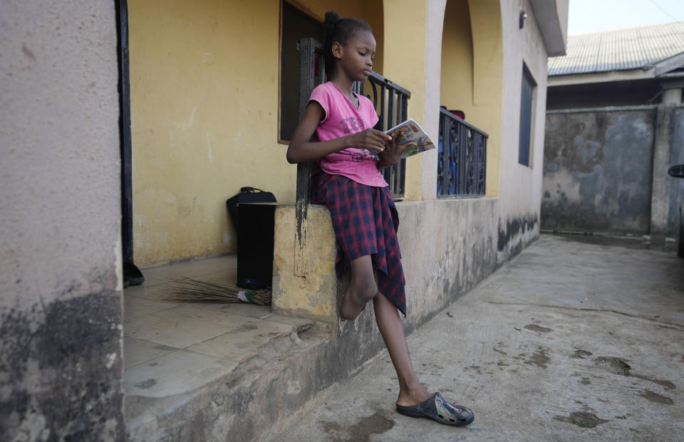 Princess Igbinosa, 10, who lost her leg following a traffic accident, reads a book outside the house she stays in with her parents in Lagos, Nigeria, Friday, Dec. 1, 2023. Princess can now walk, thanks to an artificial limb from the IREDE Foundation, a group providing children like her with free prosthetics and helping their families offset the average cost of $2,000 to $3,000. (AP Photo/Sunday Alamba)