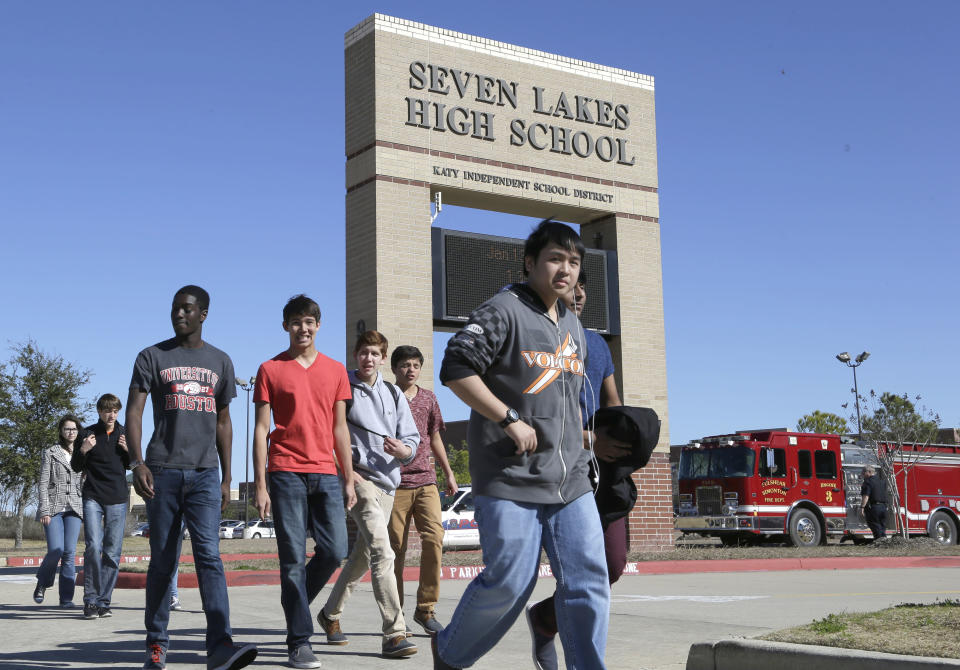 Students pass by Seven Lakes High School after being evacuated and released from school for the day Monday, Jan. 13, 2014, in Katy, Texas. A bomb squad was called to the school after a backpack with a potentially explosive devise was found. The Katy school district says a student is in custody. (AP Photo/Pat Sullivan)