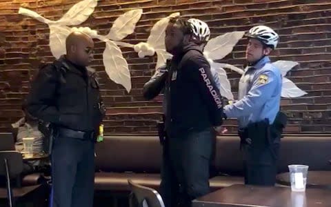 Police officers detain a man inside a Starbucks cafe in Philadelphia - Credit: Melissa Depino/via Reuters