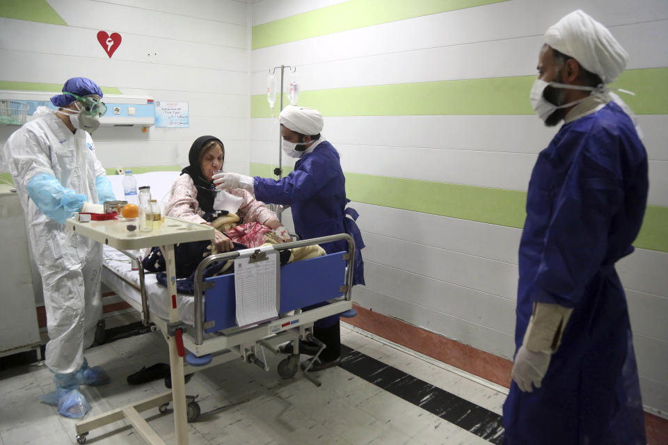 FILE — In this Saturday, March 7, 2020 file photo, a cleric, right, assists a medic treating a patient infected with the new coronavirus, at a hospital in Qom, about 80 miles (125 kilometers) south of the capital Tehran, Iran. Nine out of 10 cases of the virus in the Middle East come from the Islamic Republic. Fears remain that Iran may be underreporting its cases. Days of denials gave the virus time to spread as the country marked the 41st anniversary of its 1979 Islamic Revolution with mass demonstrations. For most people, the new coronavirus causes only mild or moderate symptoms. For some it can cause more severe illness. (Mohammad Ali Marizad/Rasa News Agency via AP, File)