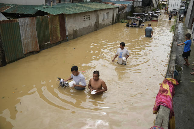 Residents carrying food packs wade along a flooded street from Typhoon Noru in San Miguel town, Bulacan province, Philippines, Monday, Sept. 26, 2022. Typhoon Noru blew out of the northern Philippines on Monday, leaving some people dead, causing floods and power outages and forcing officials to suspend classes and government work in the capital and outlying provinces. (AP Photo/Aaron Favila)