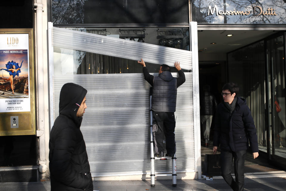 A man protects his shop a window on the Champs-Elysees avenue in Paris, Friday, Dec.14, 2018. Anticipating a fifth straight weekend of violent protests, Paris' police chief said Friday that armored vehicles and thousands of officers will be deployed again in the French capital this weekend. (AP Photo/Francois Mori)