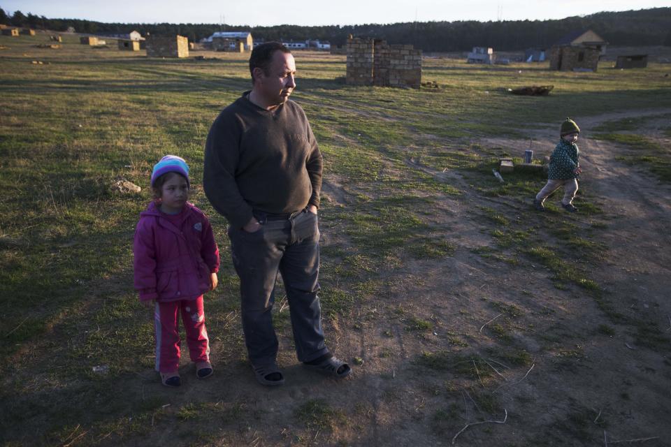 In this photo taken Thursday, March 27, 2014 Crimea's Tatar Sedomed Setumerov and his daughter Diana, left, look on as his two-year-old son Enver runs outside their recent squatter settlement in Lozovoye-2, not far from Simferopol, Crimea. On Saturday the Crimean Tatar Qurultay, a religious congress will determine whether the Tatars will accept Russian citizenship and the political system that comes with it, or remain Ukrainian citizens on Russian soil. (AP Photo/Pavel Golovkin)