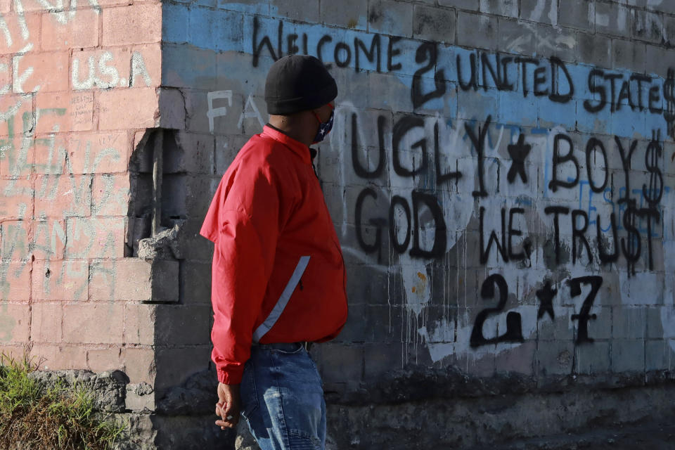 In this May 2, 2020, photo, Preston, a member of a street gang known as the Americans, passes a wall with graffiti in the Manenberg neighborhood of Cape Town, South Africa. A preacher has recruited gang members to distribute food in a violent and poor neighborhood of Cape Town during the coronavirus lockdown. (AP Photo/Nardus Engelbrecht)