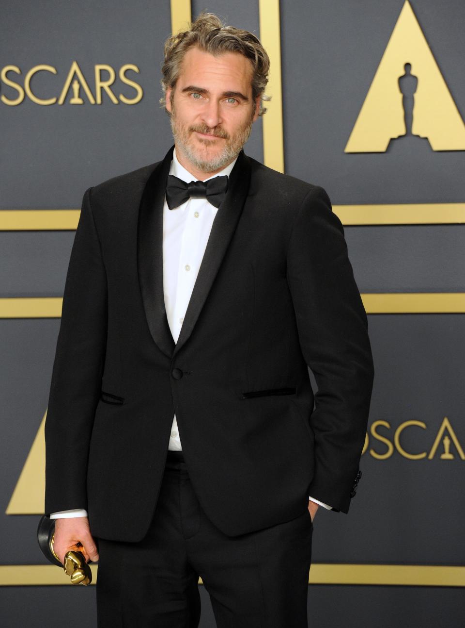 Man in a black suit and bow tie holding an award at the Oscars