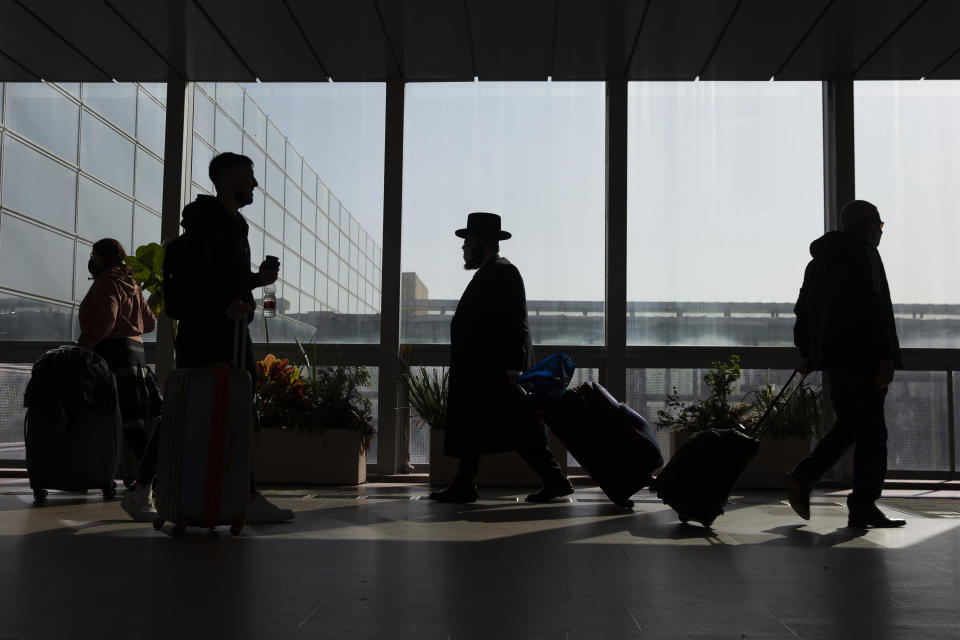 Travelers walk with their luggage in the Ben Gurion Airport near Tel Aviv, Israel, Sunday, Nov. 28, 2021. Israel on Sunday approved barring entry to foreign nationals and the use of controversial technology for contact tracing as part of its efforts to clamp down on a new coronavirus variant. (AP Photo/Ariel Schalit)