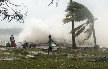 Local residents walk past debris as a wave breaks nearby in Port Vila, the capital city of the Pacific island nation of Vanuatu March 14, 2015. REUTERS/UNICEF Pacific/Handout via Reuters