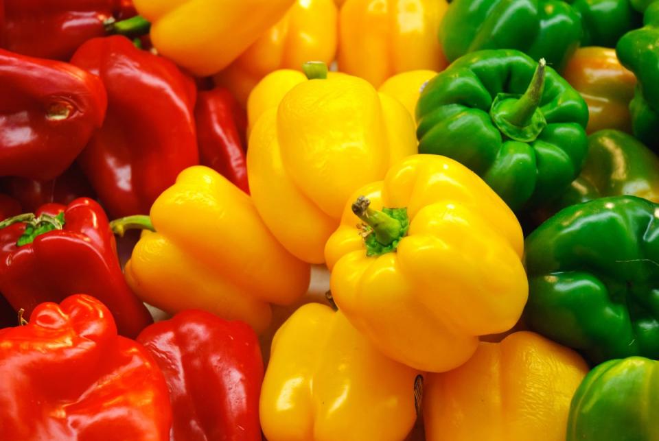 red, yellow and green bell peppers are seen stacked side by side in a farmers market display