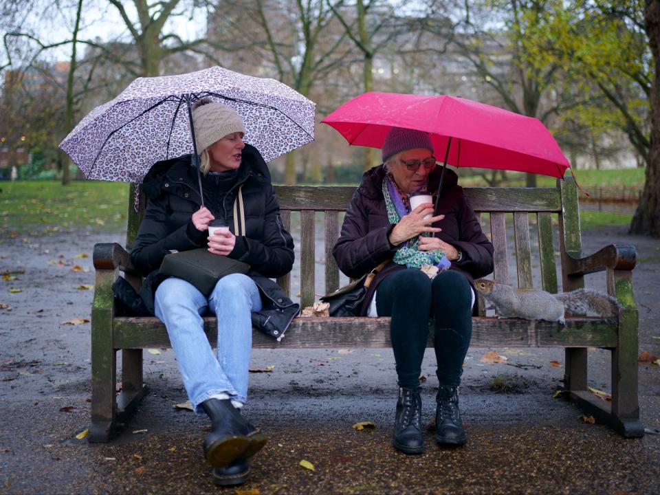 A squirrel investigates two people on a bench in St James’ Park in London amid high winds caused by Storm Barra (PA)